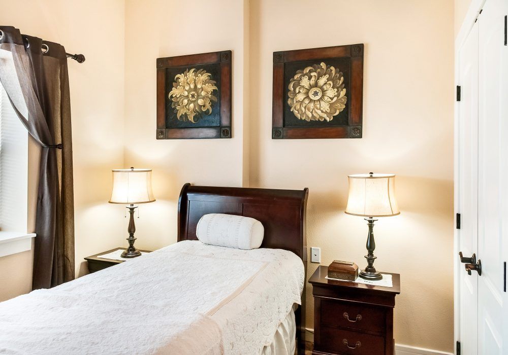 A neatly arranged bedroom with a single bed, two lamps on nightstands, and decorative wall art.