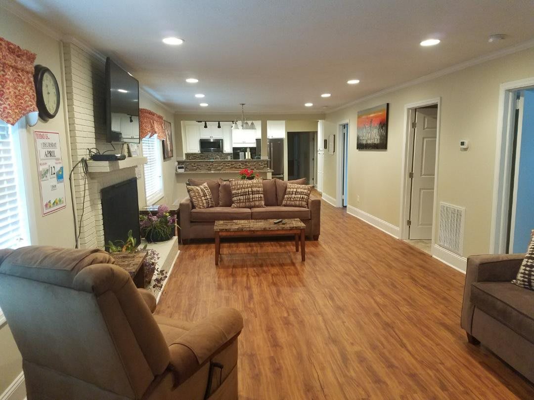 A cozy open-concept living room with a hardwood floor, featuring a couch, recliner, fireplace, and television.