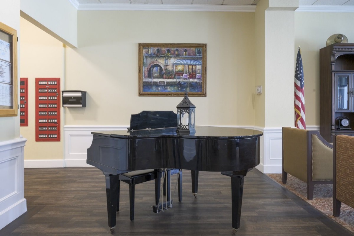 A grand piano in a room with artwork on the wall and a decorative lamp on top.