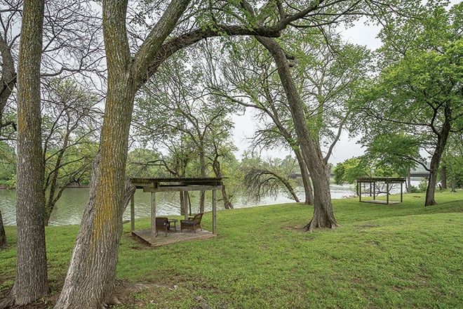 A peaceful park setting with trees and a gazebo by the river.