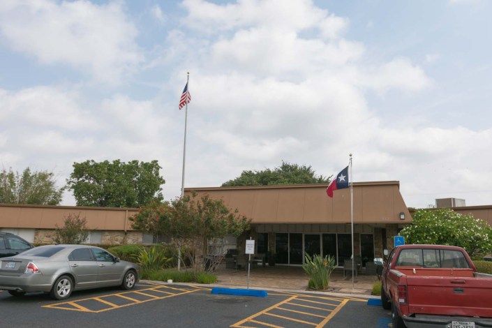 A building with American and Texas flags in a parking lot on a cloudy day.