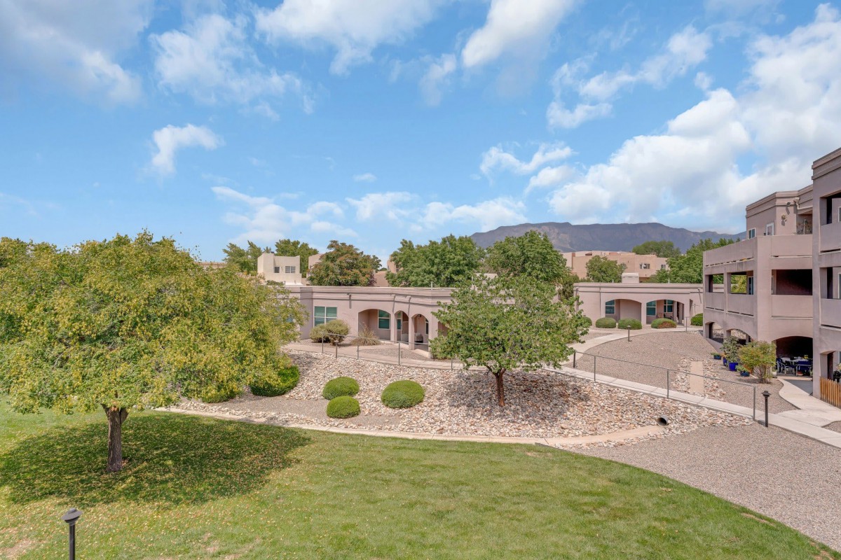 A scenic view of a house surrounded by a lush garden and under a cloudy sky.