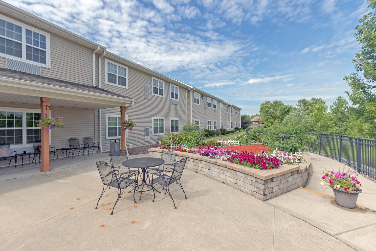 A scenic view of an outdoor patio area with garden and seating, adjacent to a building under a partly cloudy sky.