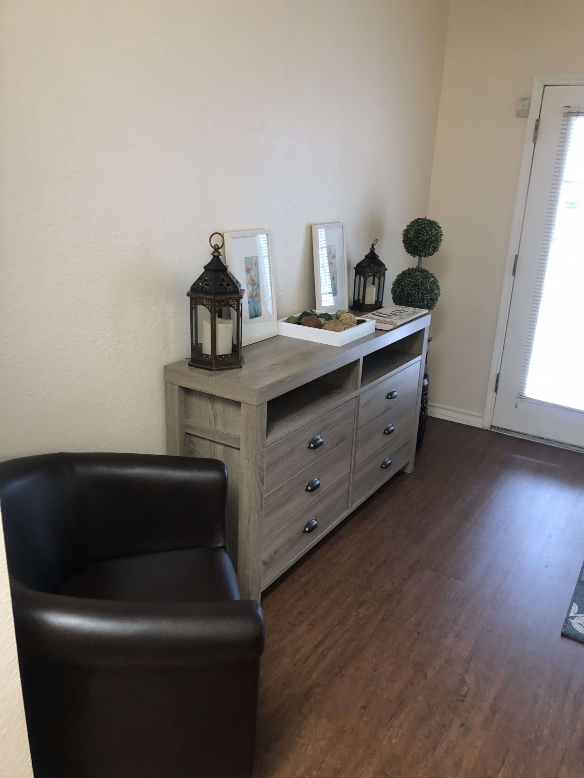 A cozy room corner with a dresser, lanterns, and a comfortable chair.