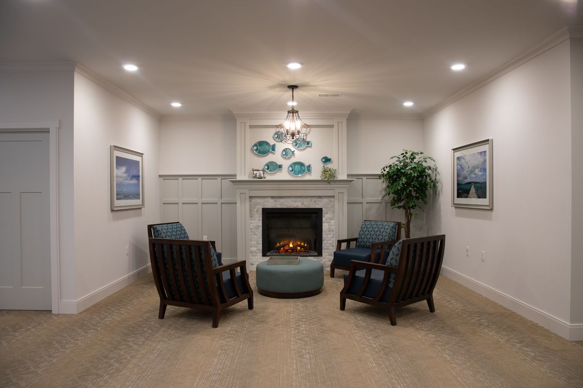 A cozy living room with a modern fireplace surrounded by four chairs and decorated with artwork and plants.