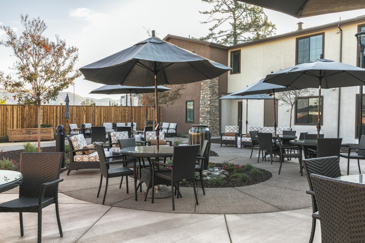 A tranquil courtyard features outdoor seating with tables, chairs, and large umbrellas.