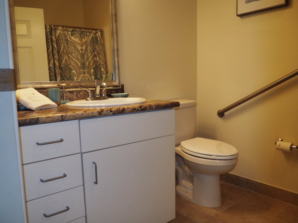 A bathroom with a toilet, sink, and counter featuring a mirror and a grab bar.