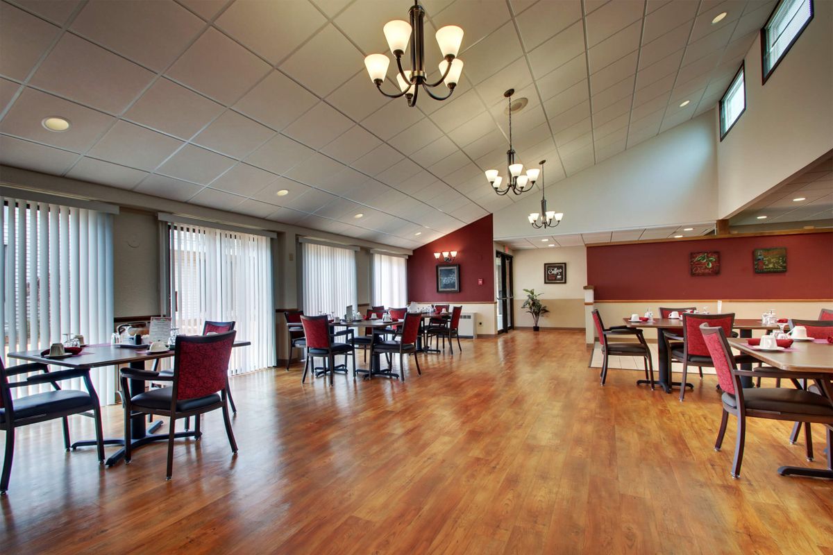 Spacious dining room with wooden floors, elegant chandeliers, and natural light streaming through large windows.