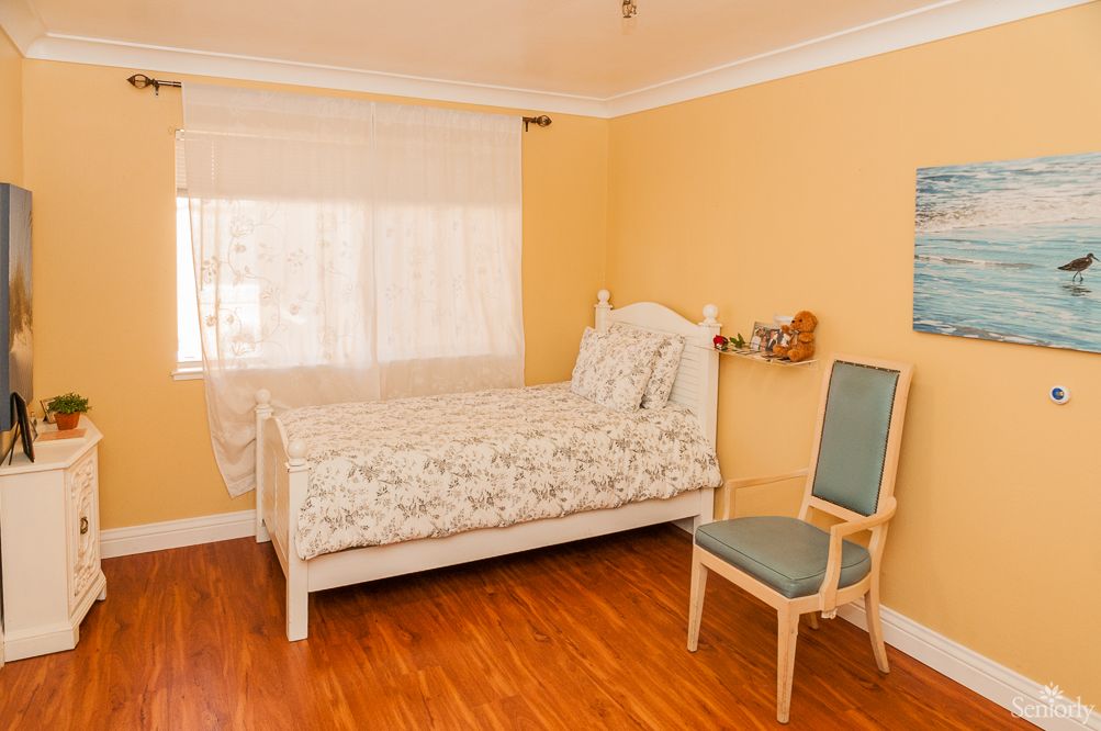 A cozy bedroom with a single bed, wooden flooring, and a chair by the window.