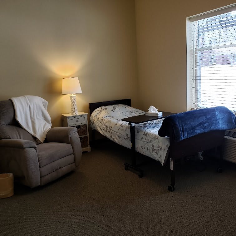 Cozy bedroom with a bed, recliner, and lamp by the window.