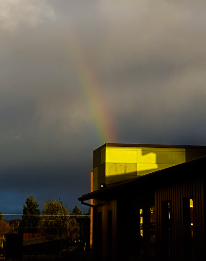 A vibrant rainbow stretches across a cloudy sky, reflecting off the surface of a building.