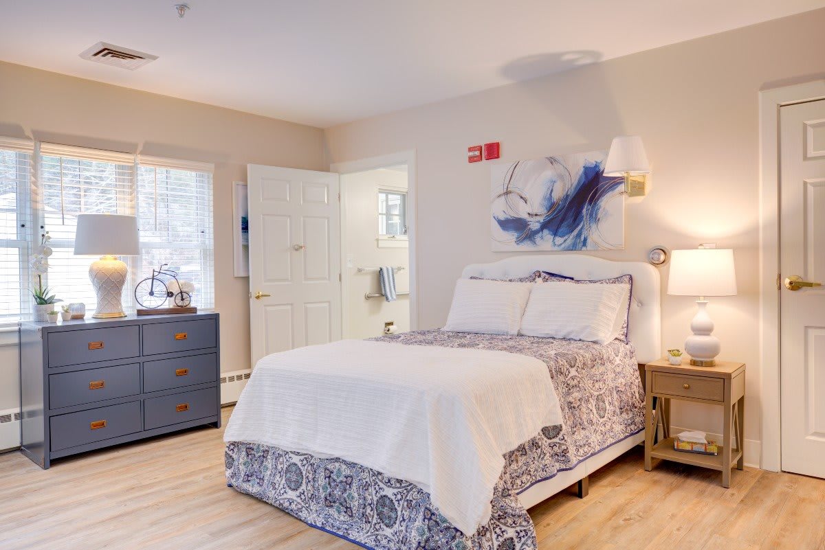 A cozy bedroom with a well-made bed, decorated with elegant linens and a bedside lamp on a wooden nightstand.