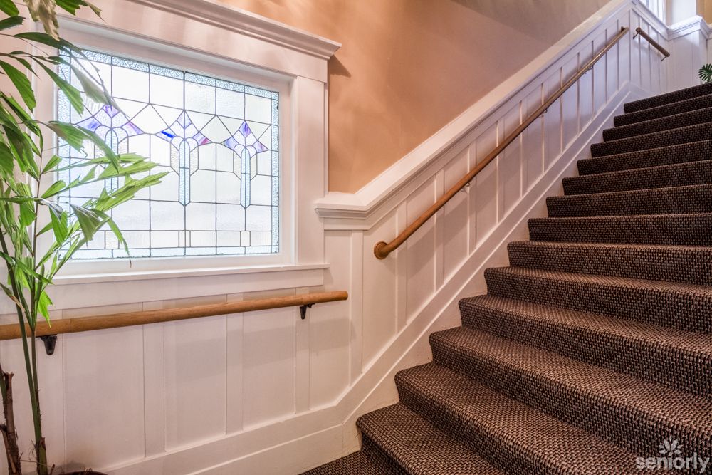 A carpeted staircase with wooden handrails beside a decorative stained glass window inside a well-lit home.