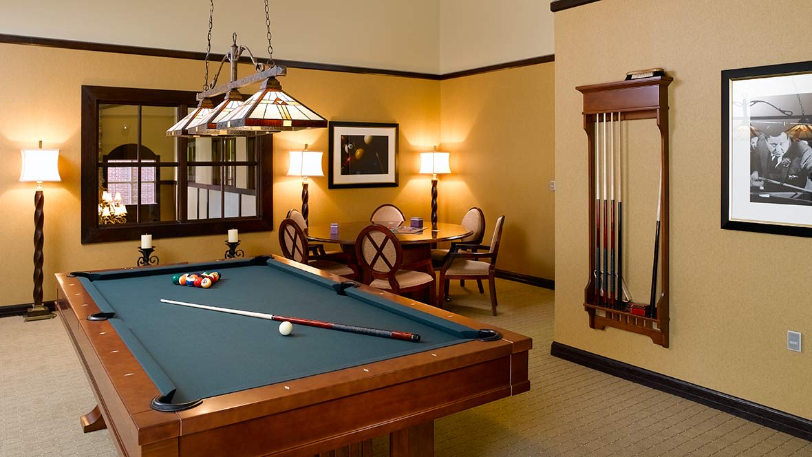 A cozy billiard room featuring a pool table, cue sticks, and a chess set on a side table surrounded by chairs.