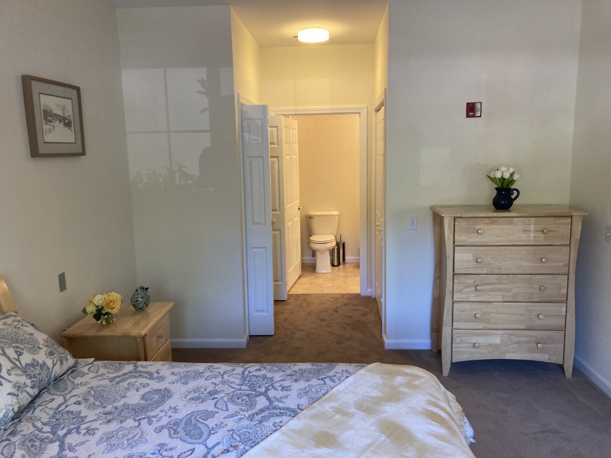 A cozy bedroom with a bed, dresser, and an open door leading to a bathroom.
