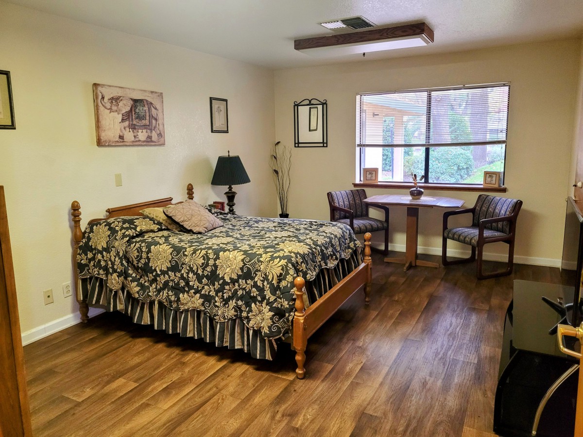 A cozy bedroom with a wooden bed, desk and chairs next to a window, and elegant decor.