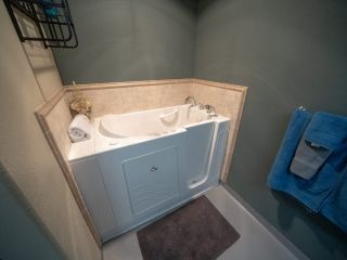 A bathroom featuring a walk-in bathtub with a handrail, surrounded by tiled walls and a towel hanging nearby.
