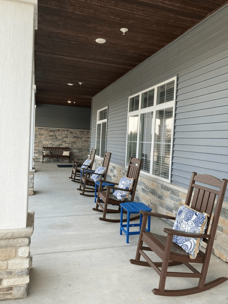 A modern porch with several rocking chairs and decorative cushions.