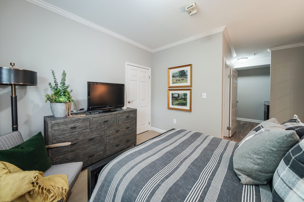 A cozy bedroom with a TV on a dresser, striped bedding, and wall artwork.