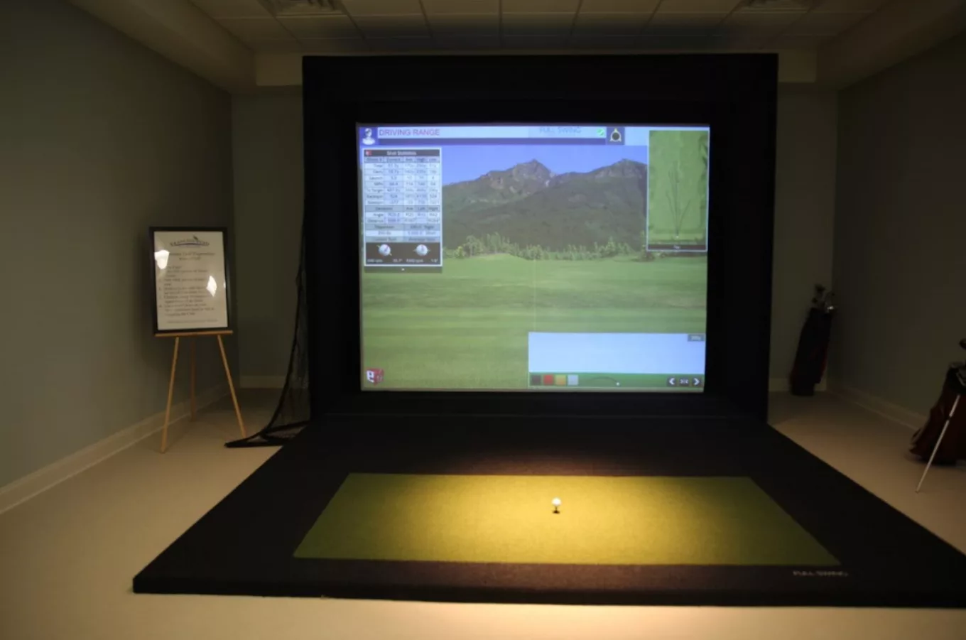 An indoor golf simulator setup with a projection screen displaying a virtual golf course.
