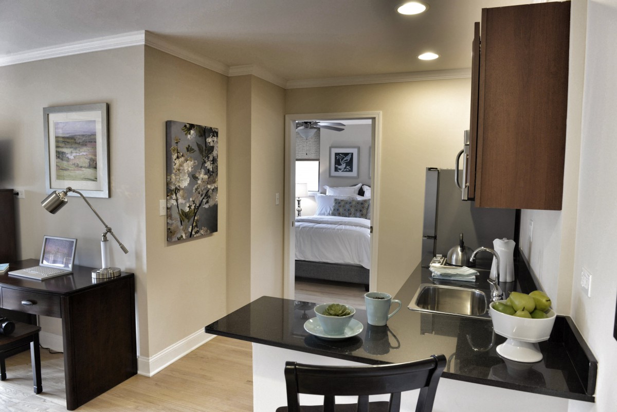 A modern kitchen area leading into a bedroom, featuring sleek countertops and stylish decor.