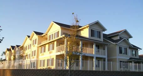 A two-story residential apartment complex with a yellow exterior, bathed in daylight.