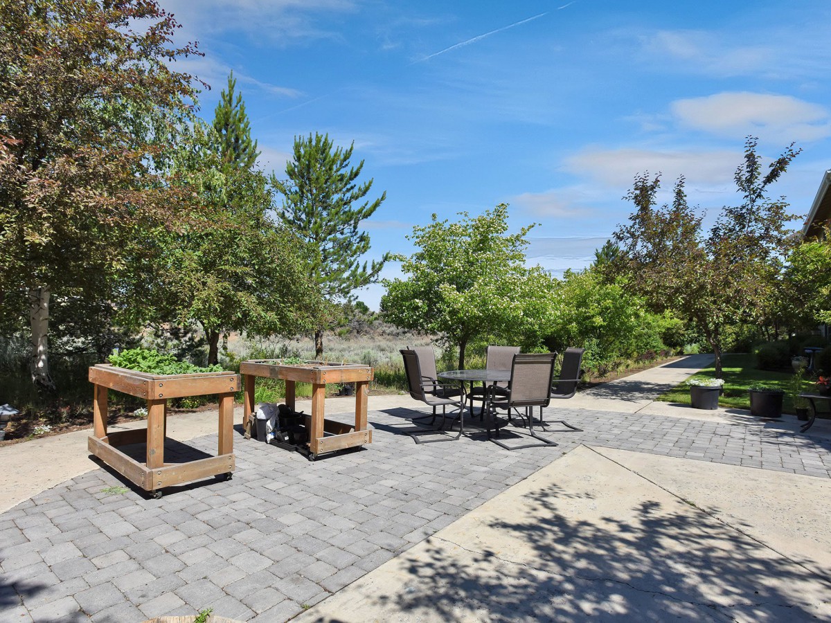 A spacious outdoor patio with furniture, surrounded by greenery and trees on a sunny day.