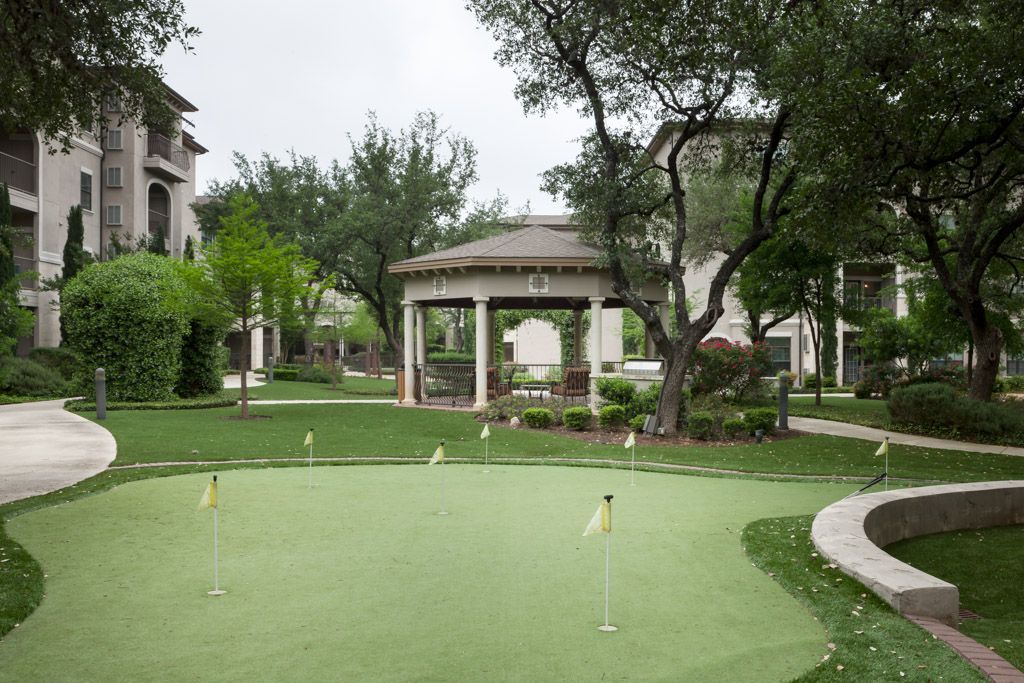A serene outdoor setting featuring a gazebo and a well-maintained putting green, surrounded by lush greenery and trees.