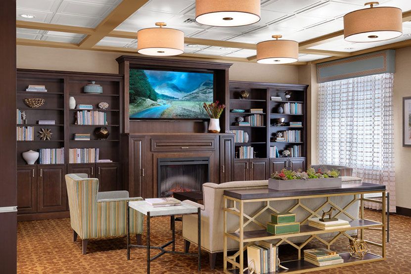 A cozy living room with modern decor featuring a television above the fireplace, bookshelves, and comfortable seating.