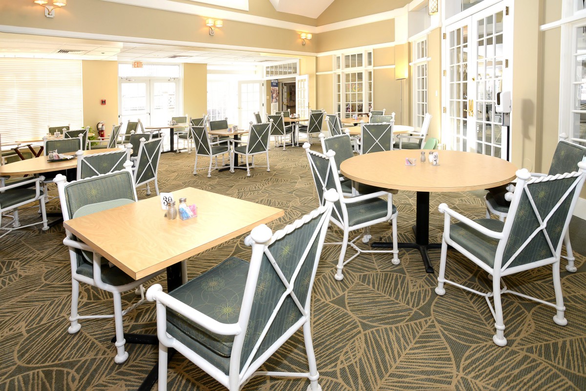 A well-lit dining area with neatly arranged tables and chairs on a carpeted floor.