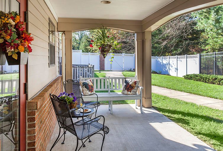 A cozy porch with a swing bench and chairs, overlooking a green garden.