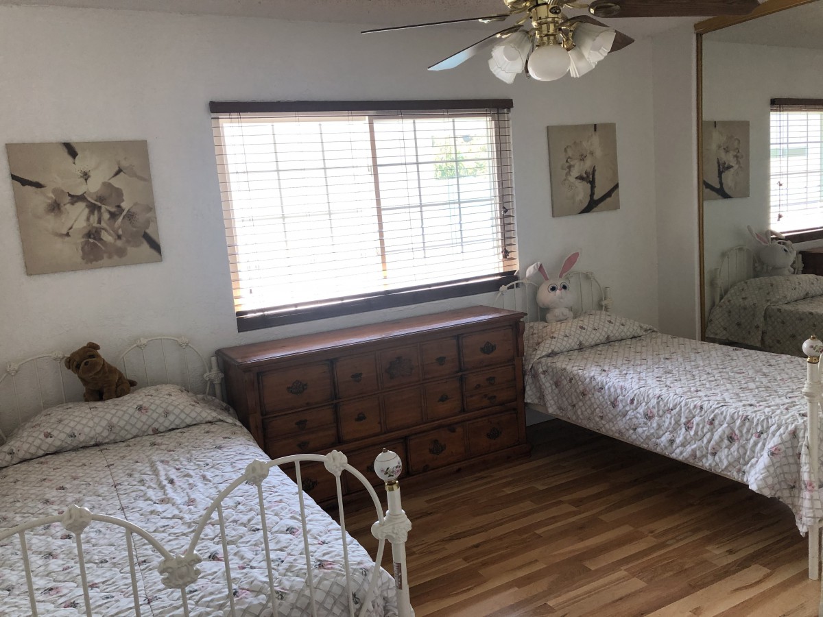 A cozy bedroom featuring two twin beds, a wooden dresser, and a ceiling fan.