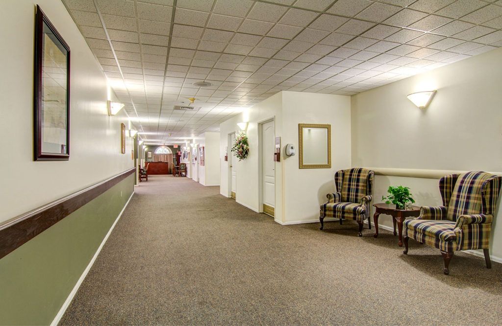 A well-lit carpeted hallway featuring armchairs and decorative elements on the walls.