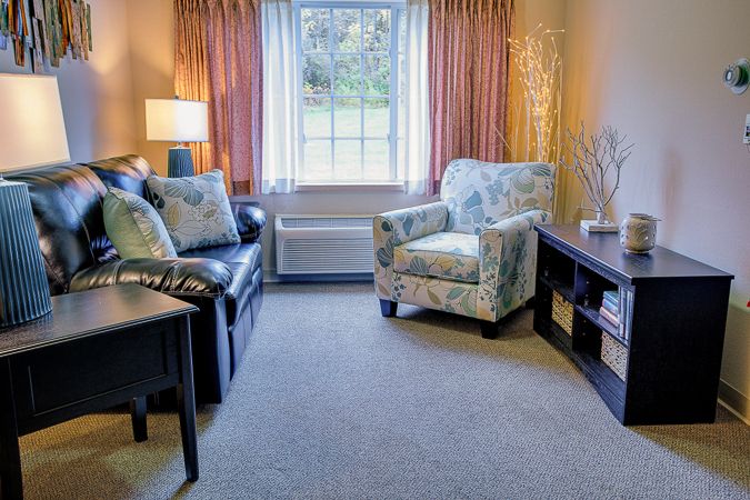 A cozy living room with a sofa, armchair, and a large window allowing natural light to fill the space.