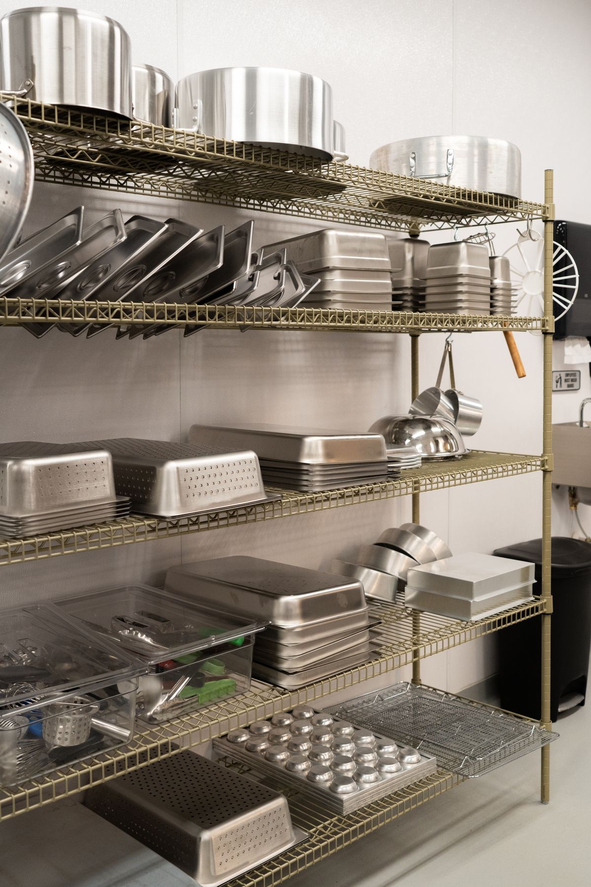 Organized metal pans and kitchenware on industrial shelves in a commercial kitchen.