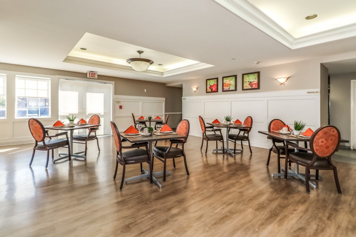 A well-lit dining area with neatly arranged tables and chairs, featuring elegant decor and a wooden floor.