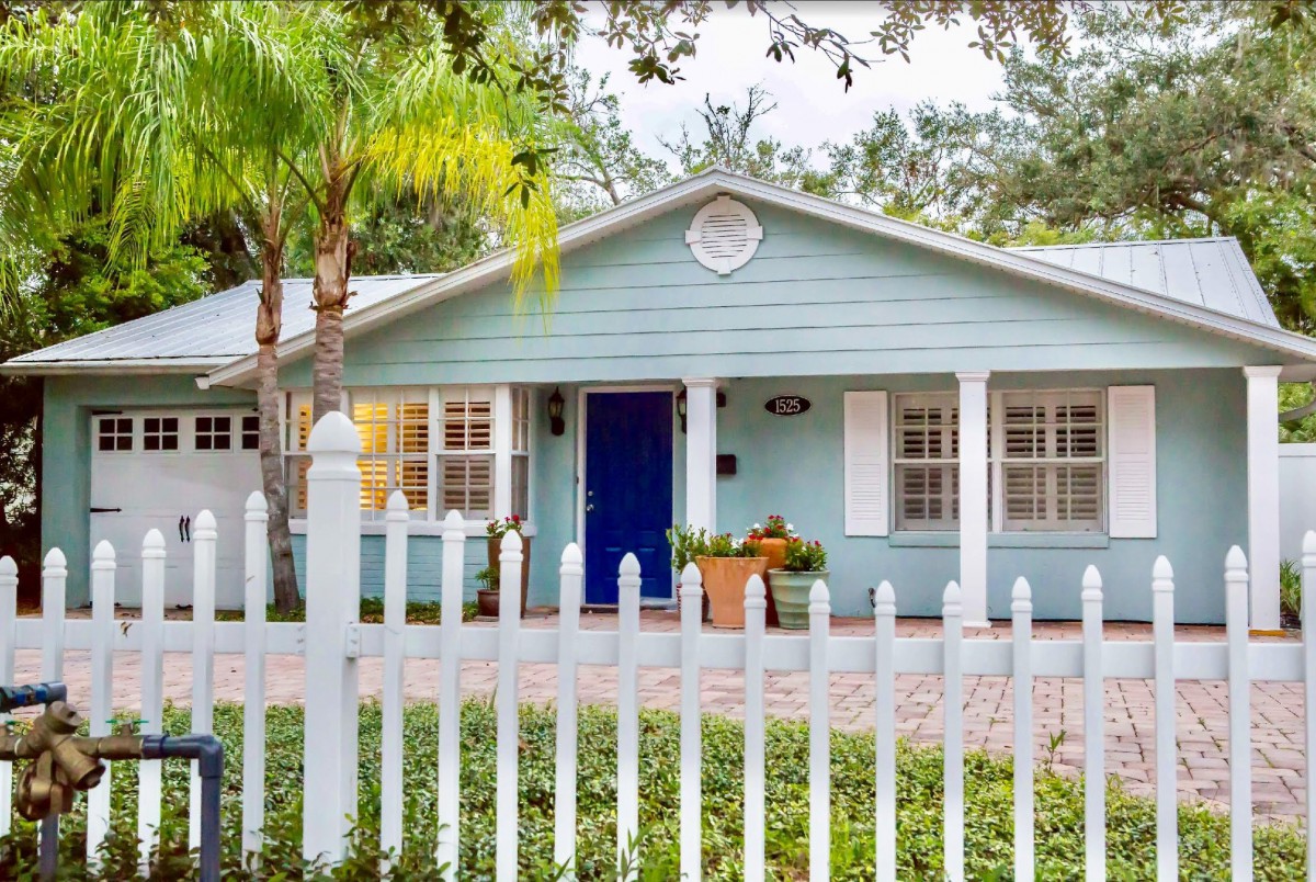 Charming blue cottage with a white picket fence and lush greenery.