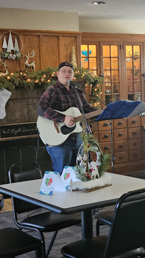 A musician performing with a guitar in a festive, decorated indoor setting.