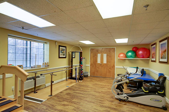 A well-equipped physical therapy room with parallel bars, a stationary bike, and exercise balls.