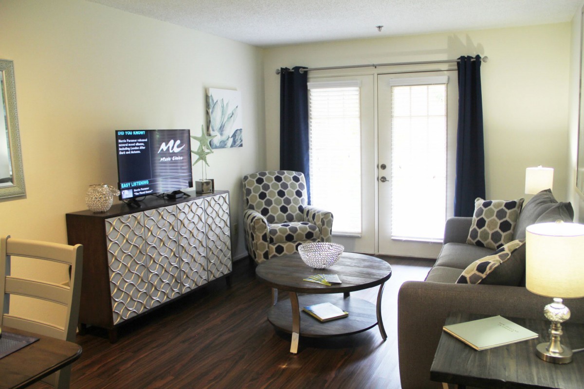 A cozy living room setup with a TV, stylish armchairs, and a sofa, complemented by dark curtains and a hardwood floor.