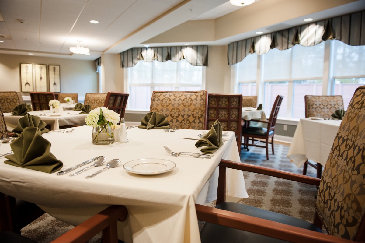 An elegant dining room with tables neatly set, featuring white tablecloths, folded napkins, and stylish decor.
