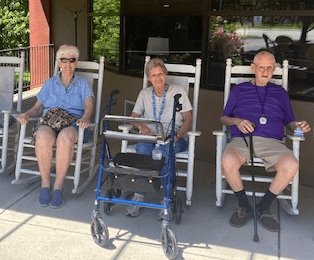 Three elderly individuals sitting outside in rocking chairs with a walker and cane nearby.