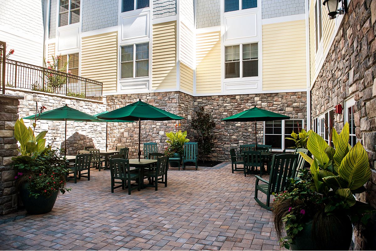 A well-furnished outdoor patio area with tables, chairs, and umbrellas in front of a building.