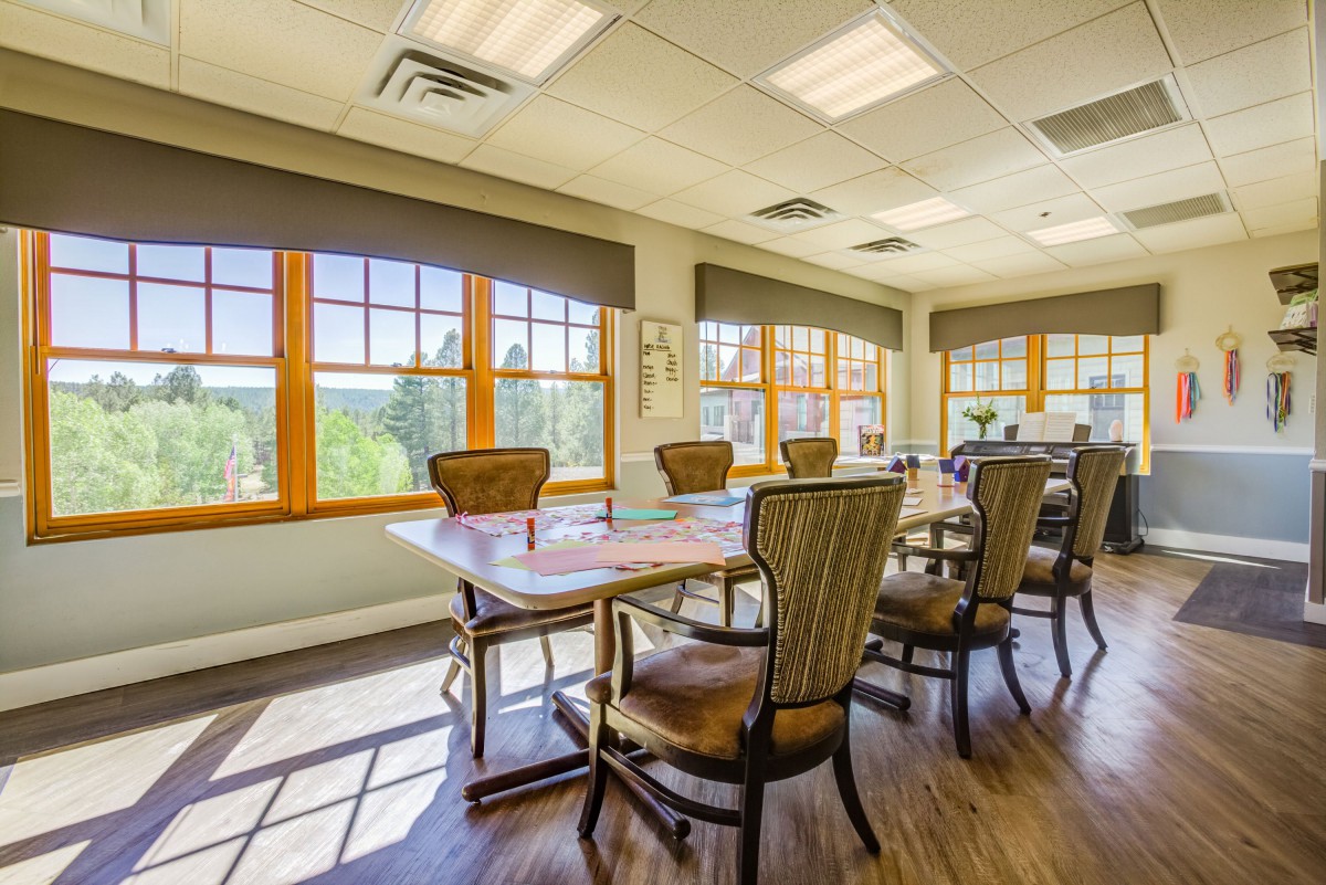 A brightly lit conference room with a large table and several chairs, featuring large windows.