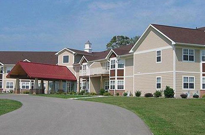 A residential building with a red roof and surrounding green lawn under a clear blue sky.