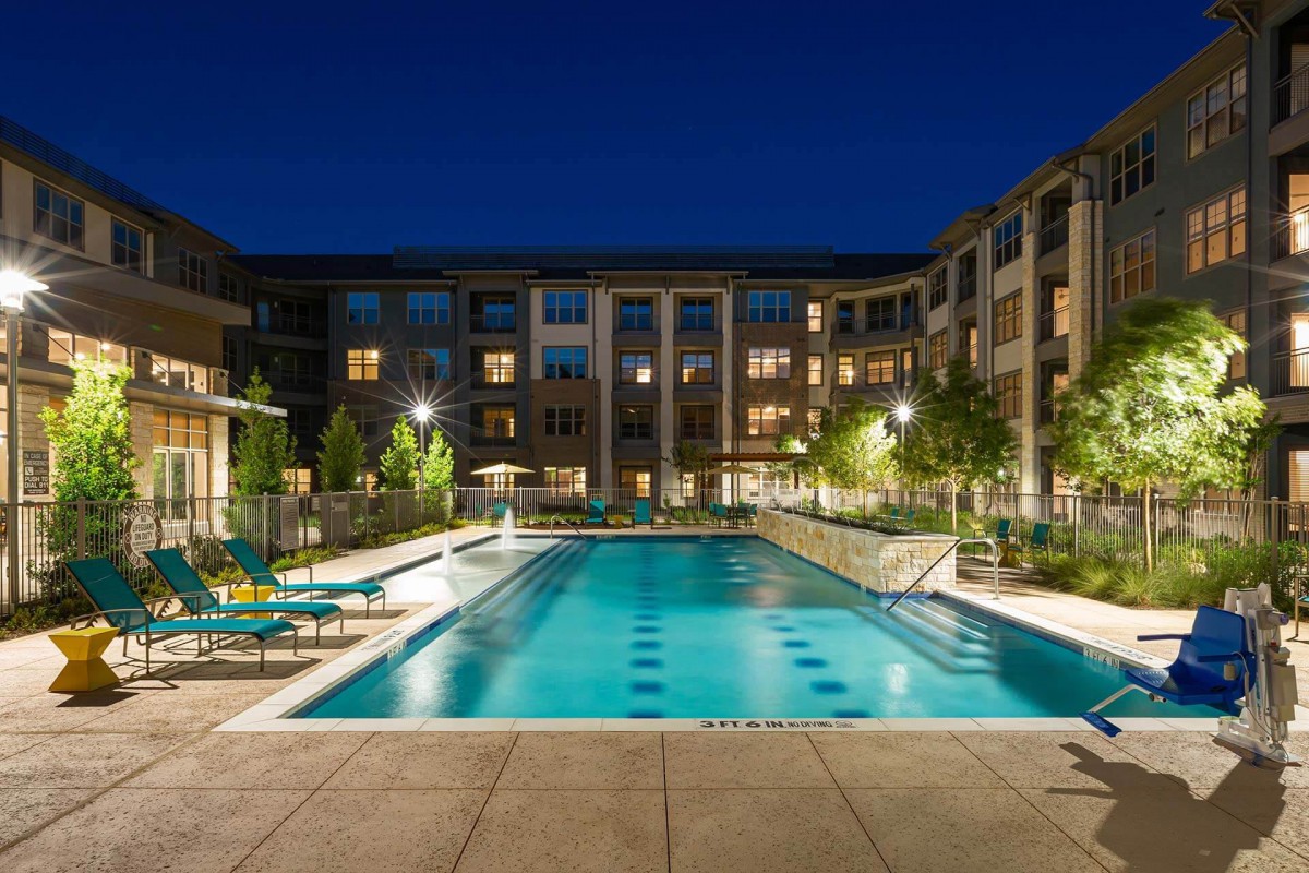 A well-lit apartment complex with a large swimming pool at night.