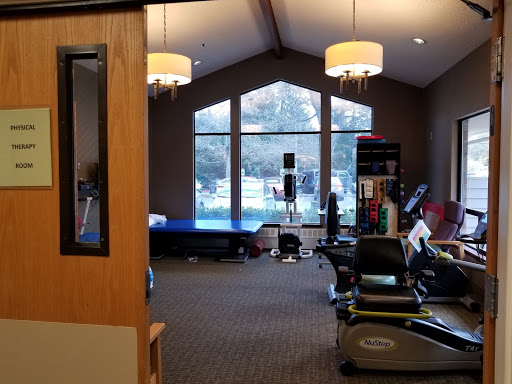 A view of a fitness center featuring various exercise equipment and large windows allowing natural light.