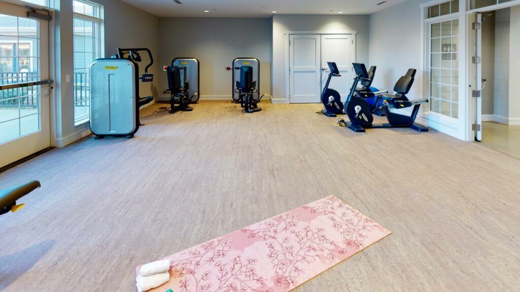 An indoor gym with exercise equipment, including cardio machines and a yoga mat.
