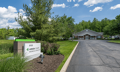 An office building with a driveway and surrounding greenery on a sunny day.