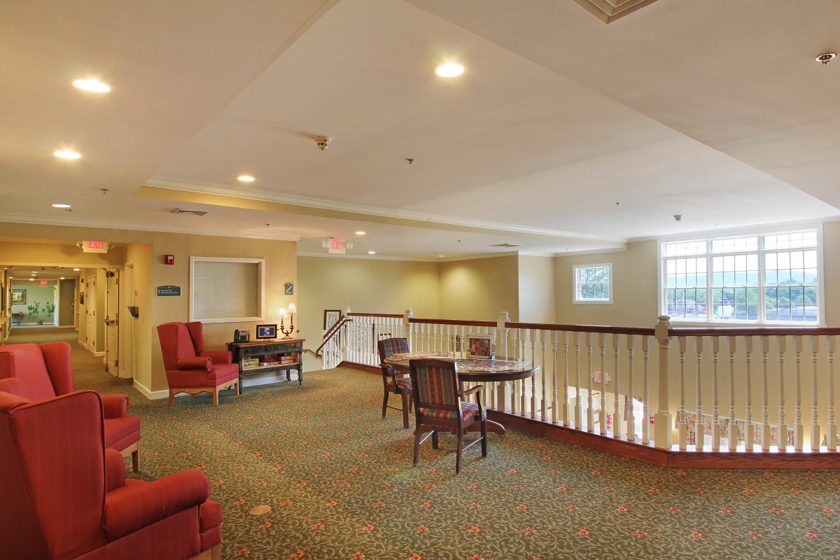 A cozy lounge area with chairs and tables, featuring carpeted floors and ample natural light.